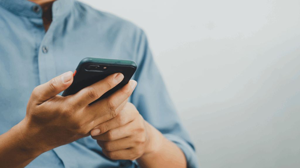 Person im blauen Hemd hält ein Smart Phone in der Hand