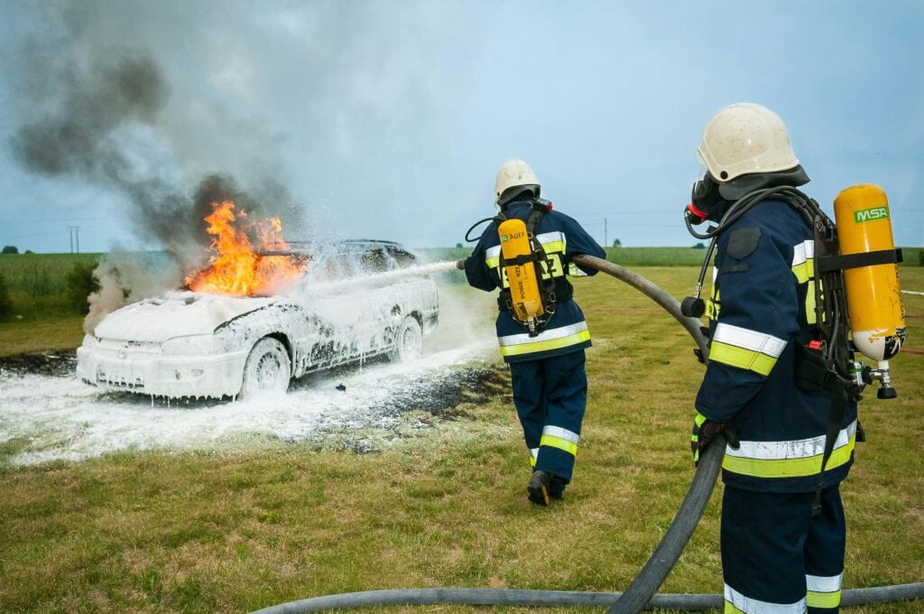 Die Feuerwehr löscht ein brennendes Auto auf einem Feld
